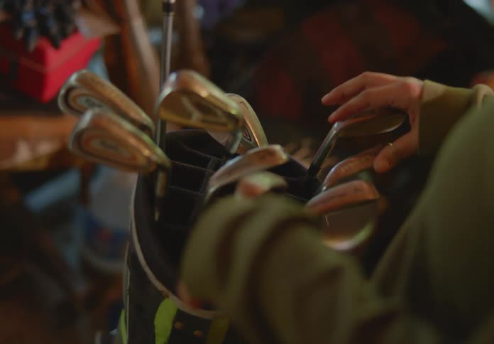 A woman touching and feeling several golf clubs as she tries to decide which one to pull from the golf bag.