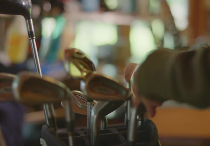 Closeup on golf clubs in a bag as a person picks them up one at time to feel their weight and balance.