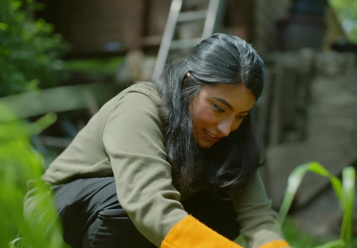 A kneeling woman uses a trowel in a garden to pull something out of the ground
