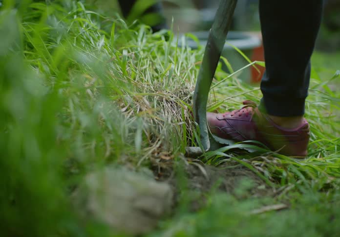 Woman with gloves and a person with hoe gardening and removing weeds from the yard