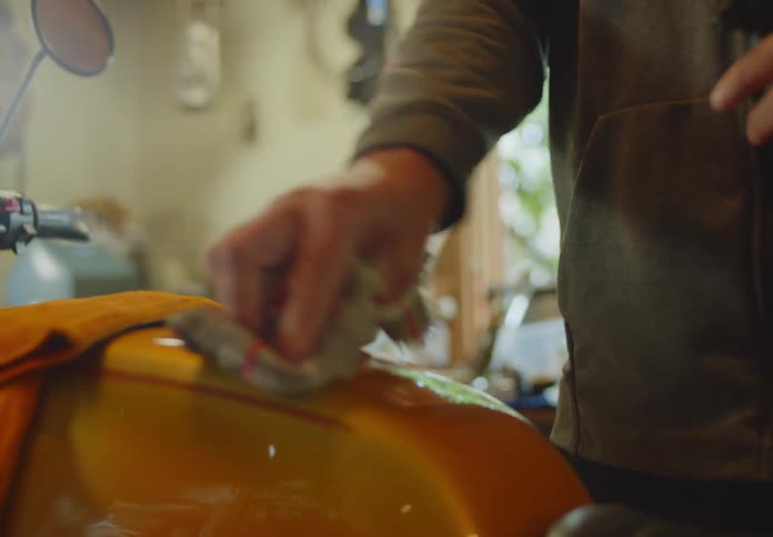 A man using a cloth and a spray to clean and polish the wheel cover of a  yellow motorcycle