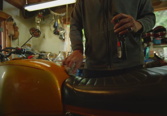 A man in his workshop polishing an orange motorcycle and enjoying his hobby.
