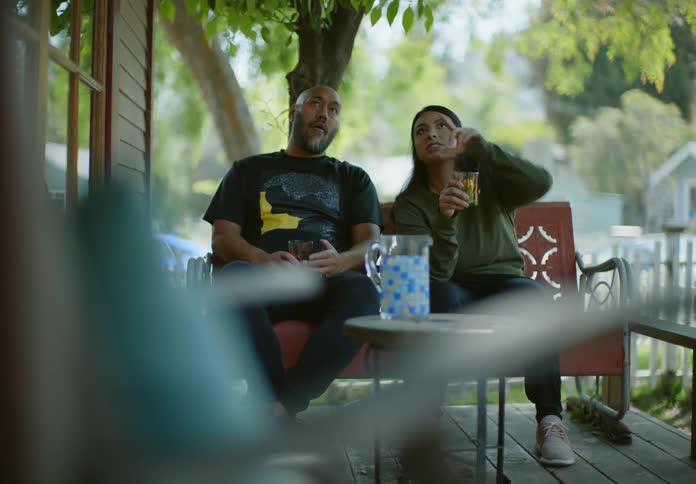 A couple seated on a red bench on a porch talking to each other