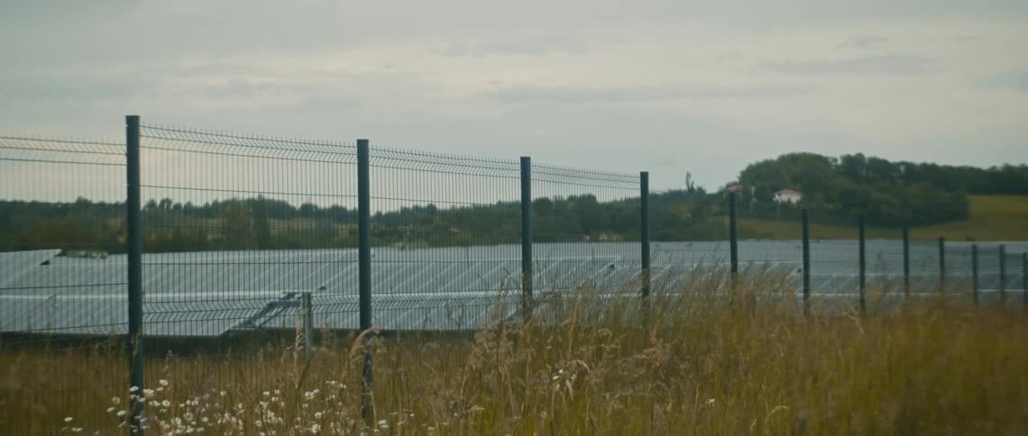 A secured solar farm with a metal fence surrounds rows of solar panels