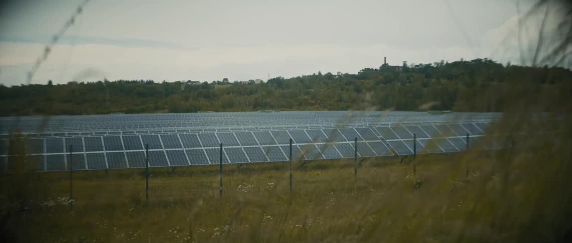 Solar panels fill a fenced in field on a windy day