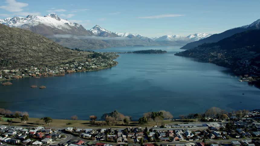Panoramic view of a lakeside town with residential areas and mountains all around