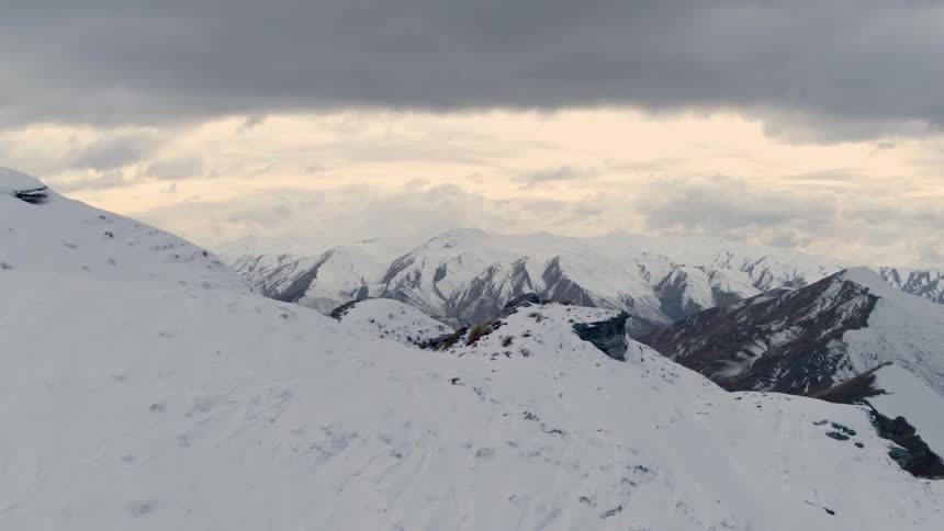 Aerial view of snow capped mountains with snow making canons peeking through a sea of clouds