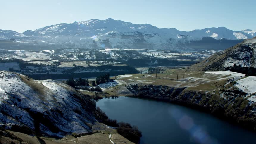 Alpine lake in Queenstown with snow covered Coronet Peak ski field mountain range blanketed in snow