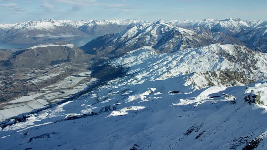 A range of mountains that are covered in white snow with lake in distance