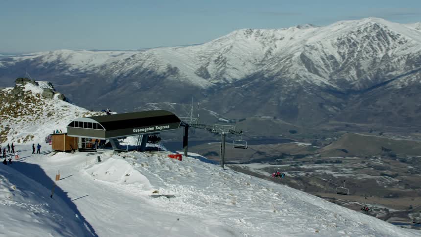 A snowcovered mountain landscape in New Zealand with a ski resort and people gathered around ski lifts