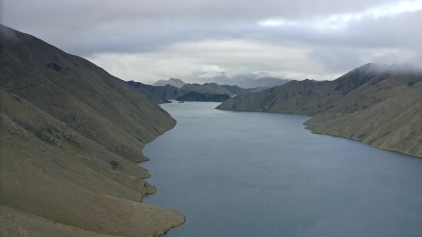 Aerial of clouds hovering over across a valley with a still lake running through it