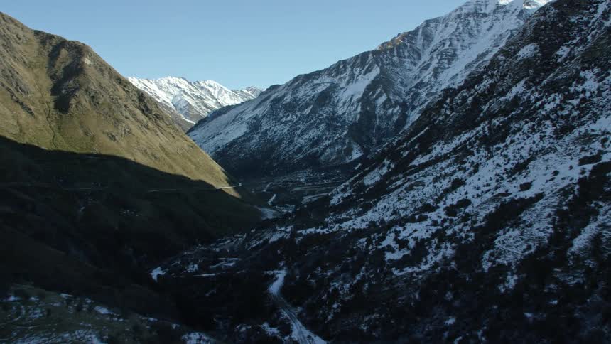 Mountainous valley with steep slopes and snowcapped peaks alongside other mosscovered mountains