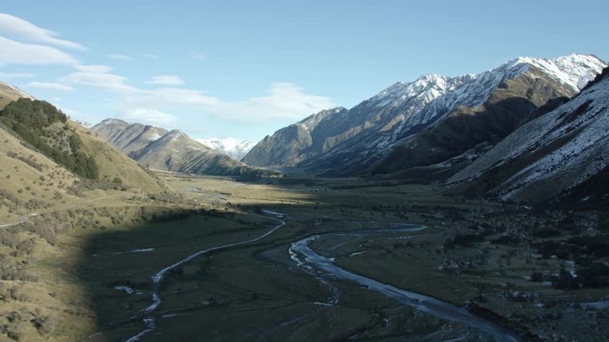 Road runs along side of mountain over valley with multiple waterways during winter