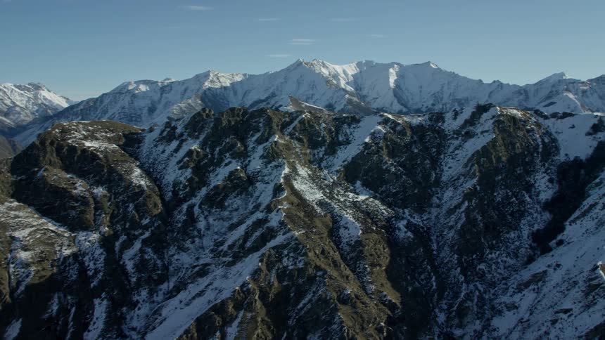 Vast mountain range with sharp peaks some covered in snow and a strong sun on a clear day