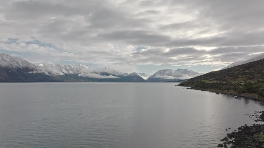 A large lake with a rocky shore in front of a mountain range