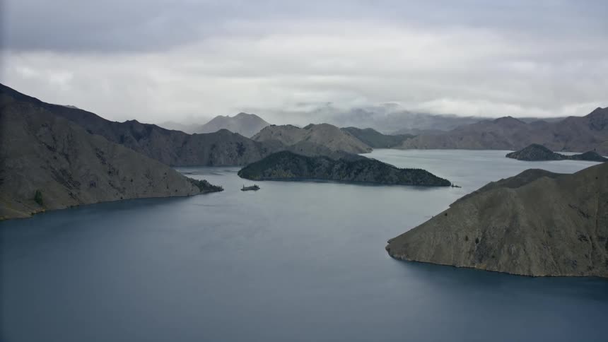 Long tracking aerial across a large lake surrounded by moody mountains