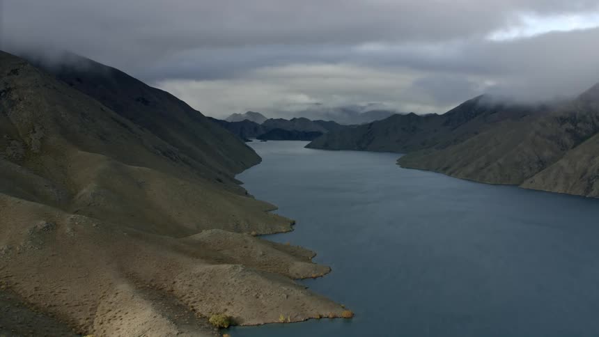 The lake is calm by the mountains with a storm approaching in the distance