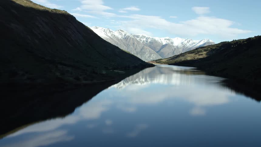 Reflective alpine lake is at the top of the mountain in shade with reflected mountain and snow