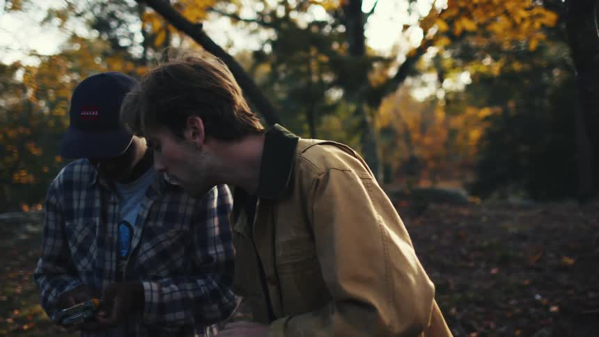 Two young men load film into their cameras at sunset