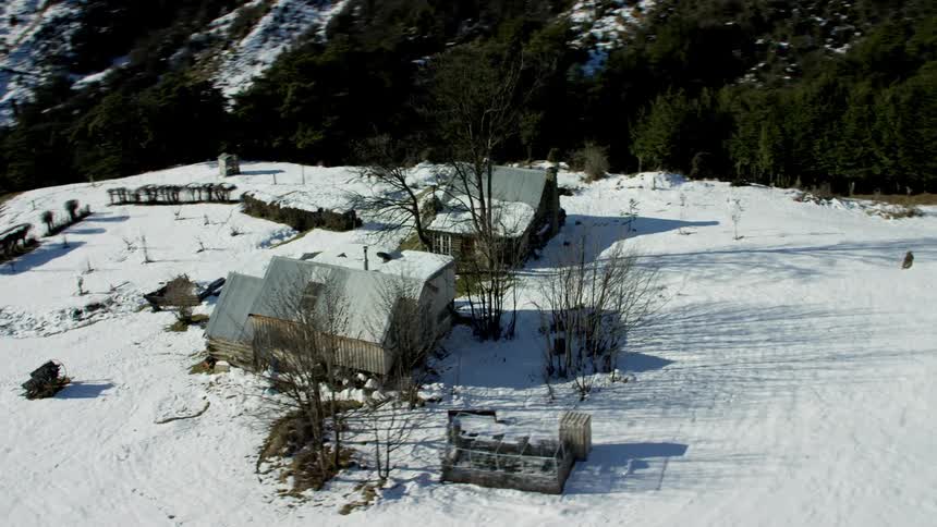 An aerial view shows a lone farmhouse nestled amongst snowcovered fields in a mountainous area