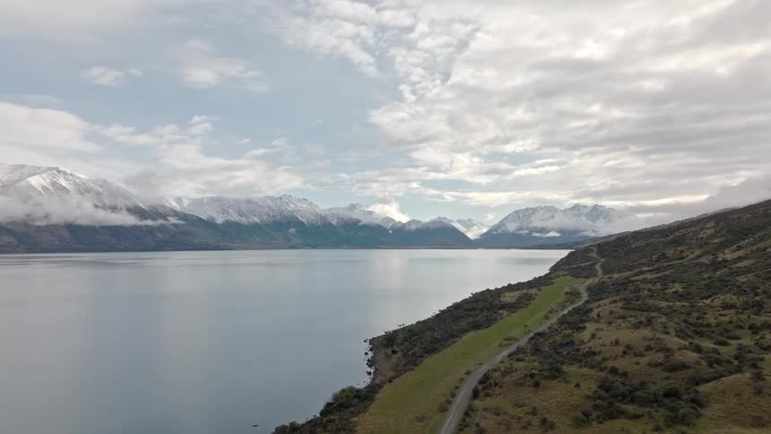 A large lake is by the mountains with a small vehicle track beside