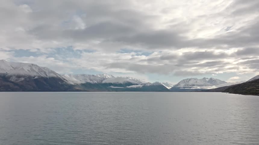 Serene lake surrounded by snowcapped mountains under a cloudy sky