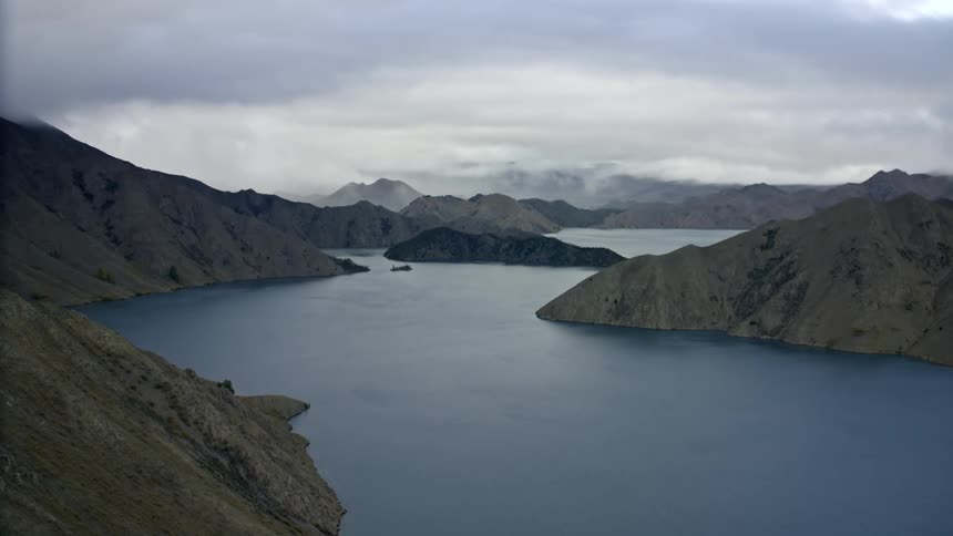 Dramatic aerial of a brewing storm in the distance above a lake surrounded by mountains