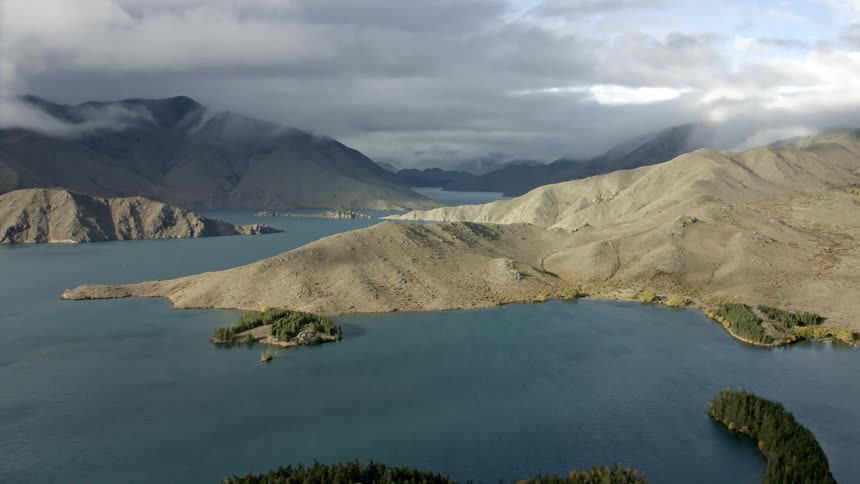Very long stable tracking shot across a large body of water with several islands and peninsulas surrounded by mountainous terrain
