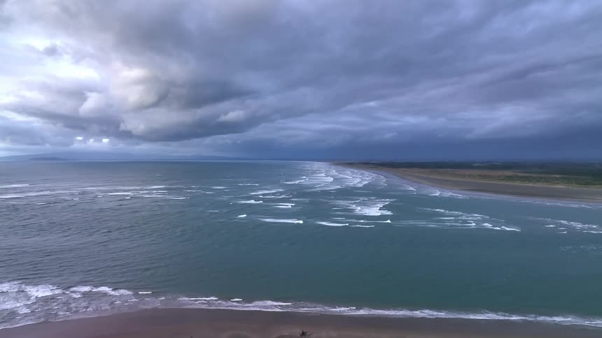 Waves foam while rolling toward beach under gray storm clouds