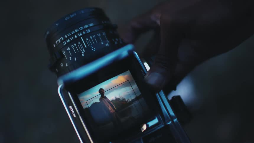 Hand adjusting the lens of a camera focused on a man in nature