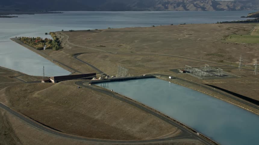 Hydroelectric power plant on river leading into lake with mountains in distance