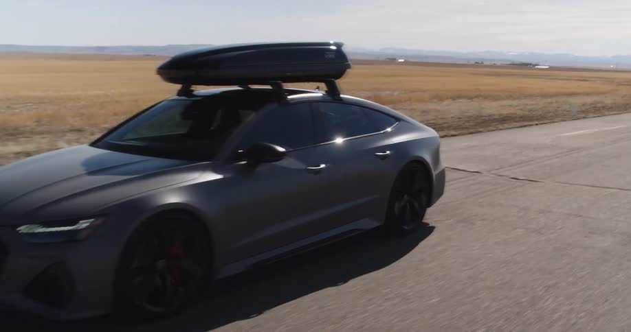 Gray car with a luggage box on the roof driving on a road
