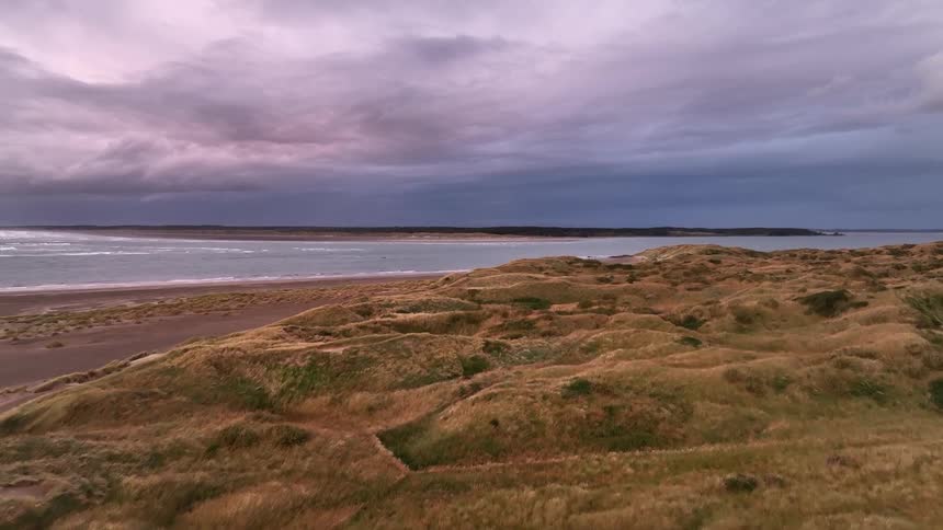 A coastal landscape with a grassy field in the foreground and a calm sea and dark storm clouds