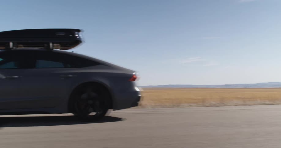 A car with a roof box driving on a road next to the desert