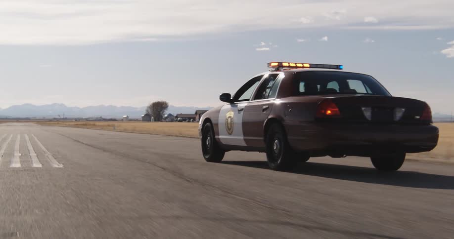 A police car is swerving all over the road on the street in an empty grassland area