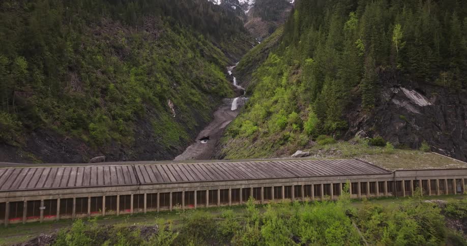 Long covered bridge nestled in a lush green mountain landscape with a flowing river