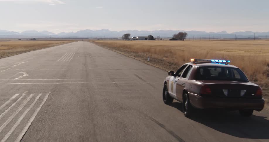 Police car in motion with emergency lights on on a paved road with fields and mountains in the background