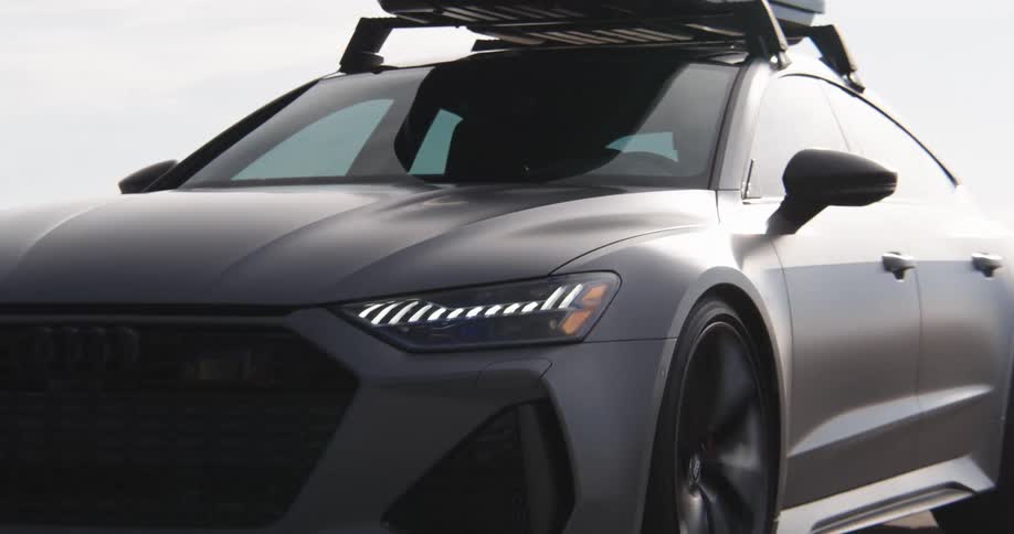 An audi rs 6 station wagon with a black roof rack drives down a scenic road