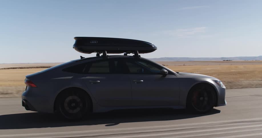 Gray sports audi drives on an empty road surrounded by open fields