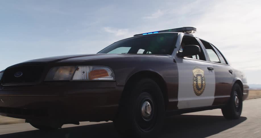 A police car with the giroflex turned on and driving on a wide asphalt street