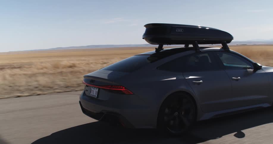 A sports car with a luggage on top driving on a road in a desert region