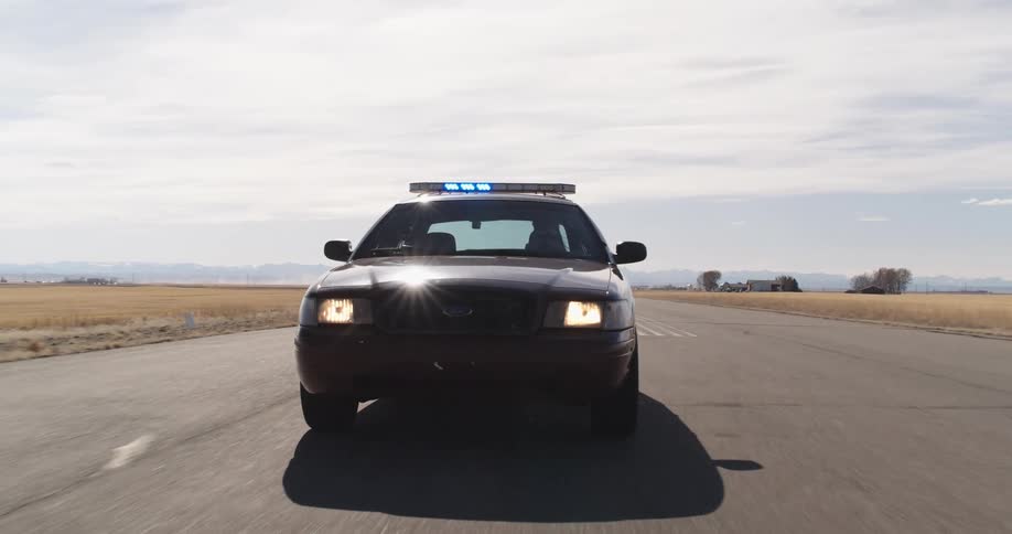 A police car with the siren on driving on an asphalt street in a rural region