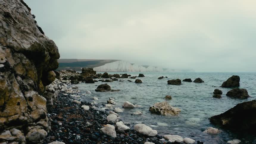 The edge of an ocean is washing up onto the shore filled with many rocks and stones
