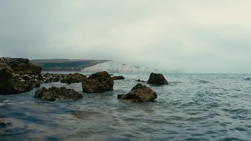 Small ocean waves wash up onto the shore scattered with rocks