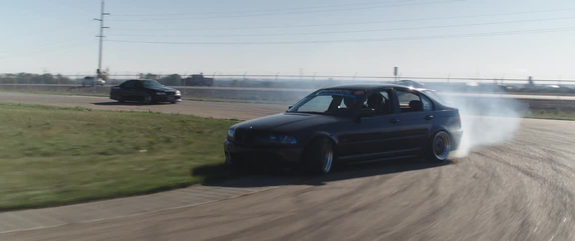 Multiple cars speed around a racetrack on a sunny day