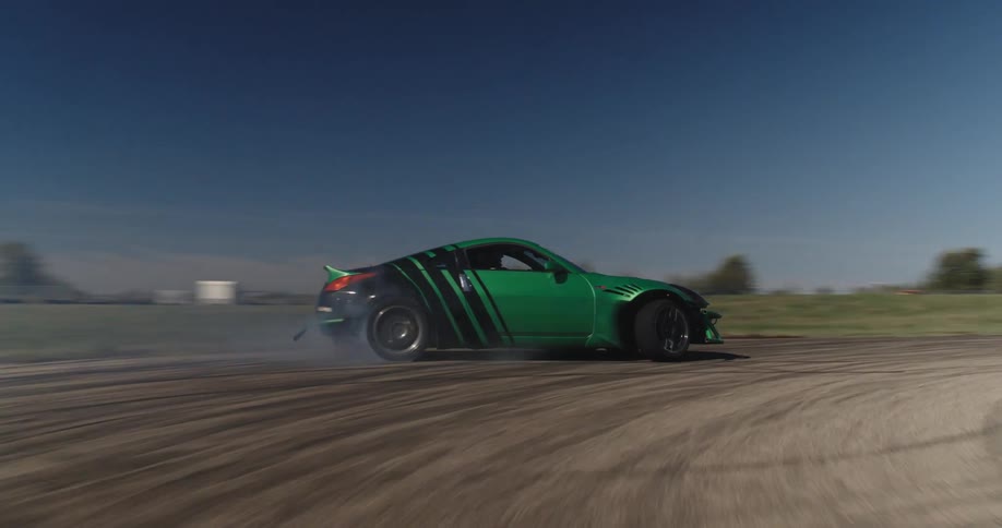 Aerial view of a green race car drifting on a track leaving a trail of smoke