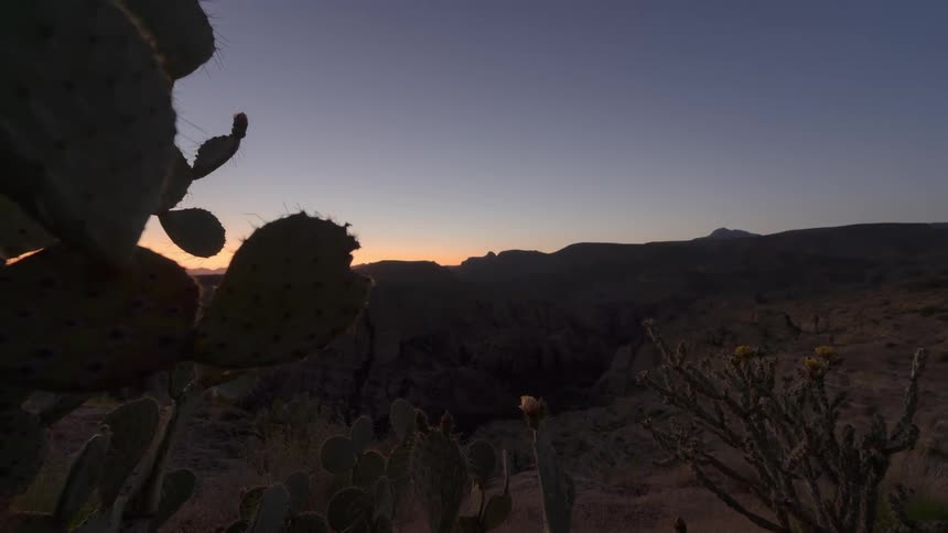 Sun sets and Aurora appears in night sky over arid canyon in desert terrain