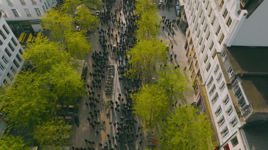 Aerial view of a city street with buildings where a large group of people are walking in a demonstration