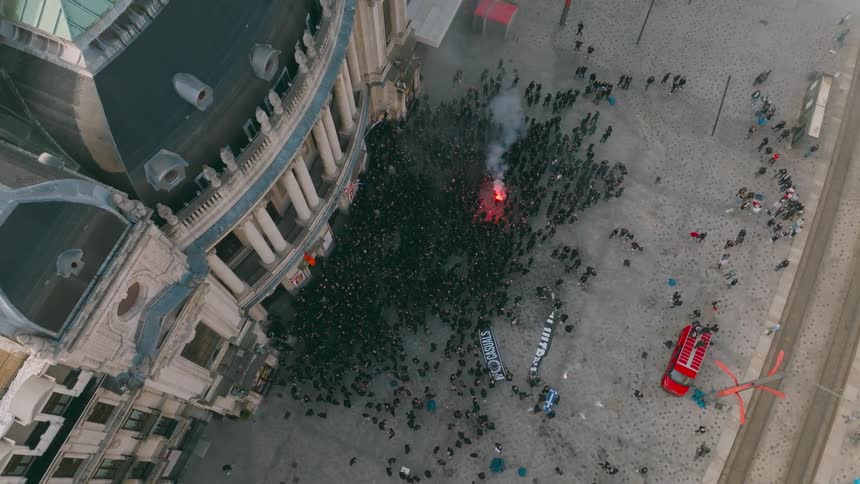 Aerial view of a crowded public square with people gathered around a red traffic light