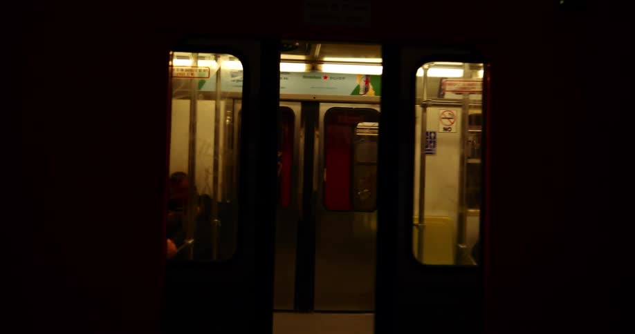A dark subway station with a train stopped at the platform opening its doors